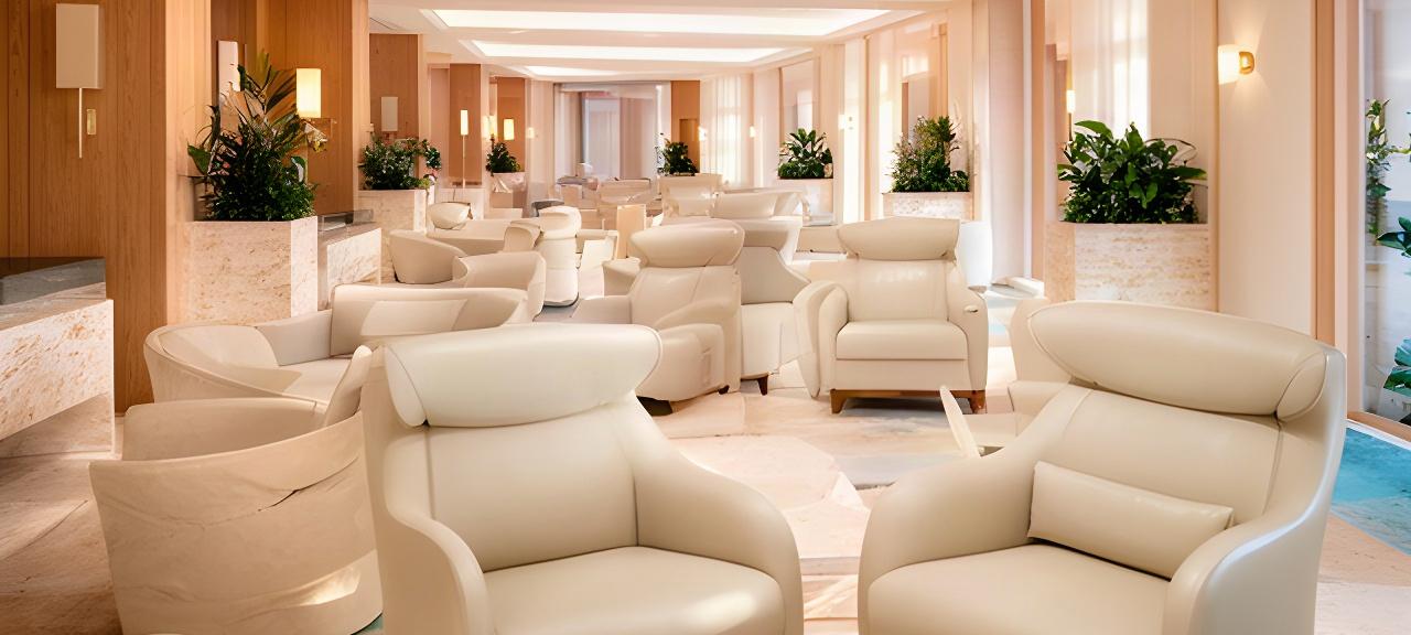 Area lounge di una spa con poltrone in pelle chiara, luci soffuse e dettagli in legno naturale